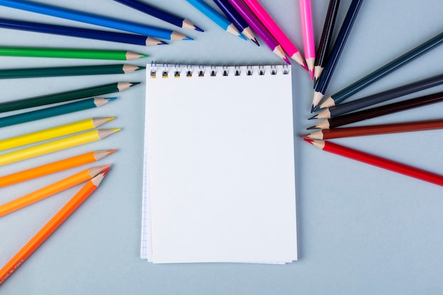 Top view of a sketchbook with colored pencils arranged around on white