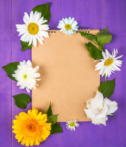 Top view of a sketchbook with daisy and gerbera flowers on purple wooden background