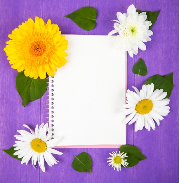 Top view of a sketchbook with daisy and gerbera flowers on purple wooden background