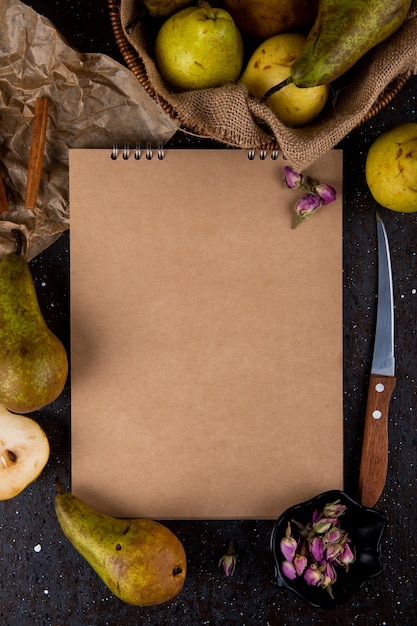 Top view of sketchbook with fresh ripe pears kitchen knife and cinnamon sticks on black background