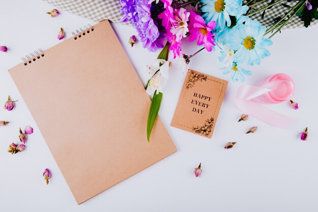 Top view of a sketchbook with a postcard and colorful chrysanthemum flowers bouquet on white background