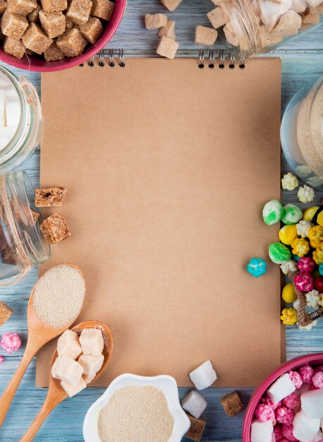 Top view of a sketchbook with various types of sugar and candies in bowls and glass jars arranged around on rustic background
