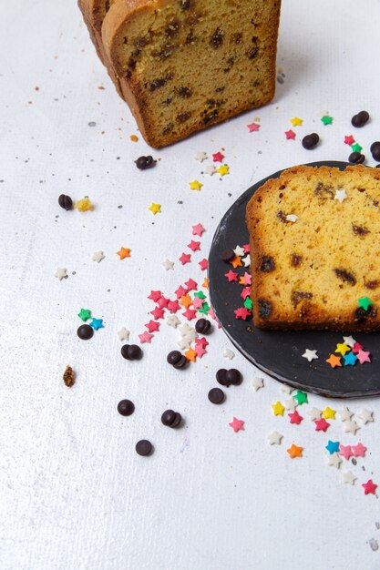 Top view slice of cake inside dark plate with colorful candies on the light background cake sugar biscuit bake