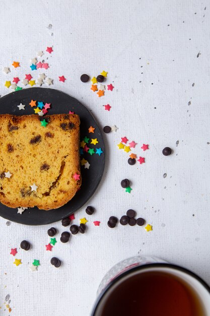 Top view slice of cake inside dark plate with colorful candies on the light background cake sweet sugar bake