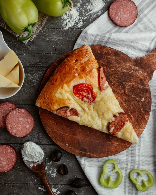Вид сверху на кусок пиццы с пепперони, томатным перцем и сыром