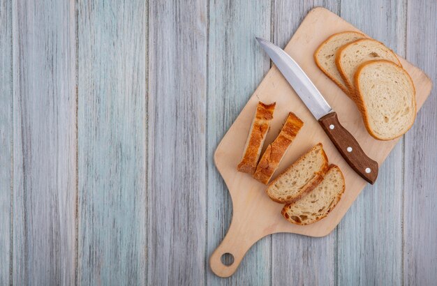 Top view of sliced baguette and knife on cutting board on wooden background with copy space