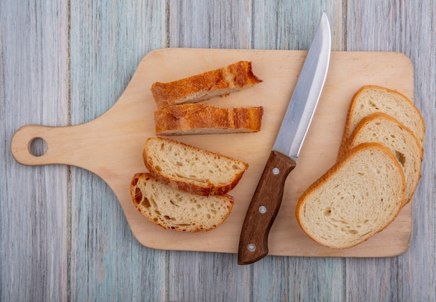 Free photo top view of sliced baguette and knife on cutting board on wooden background