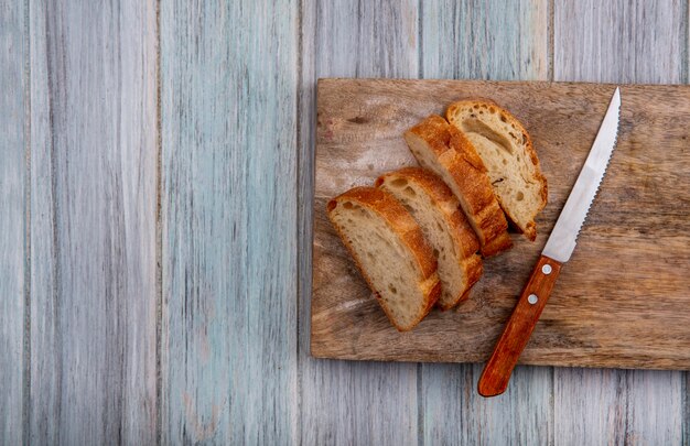 Top view of sliced baguette with knife on cutting board on wooden background with copy space