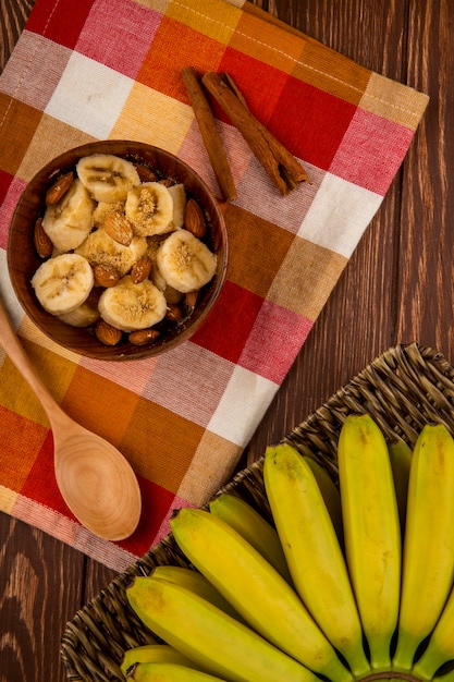 Free photo top view of sliced bananas with almond in a wood bowl and bunch of fresh bananas in a wicker basket on rustic