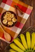 Free photo top view of sliced bananas with almond in a wood bowl and bunch of fresh bananas in a wicker basket on rustic