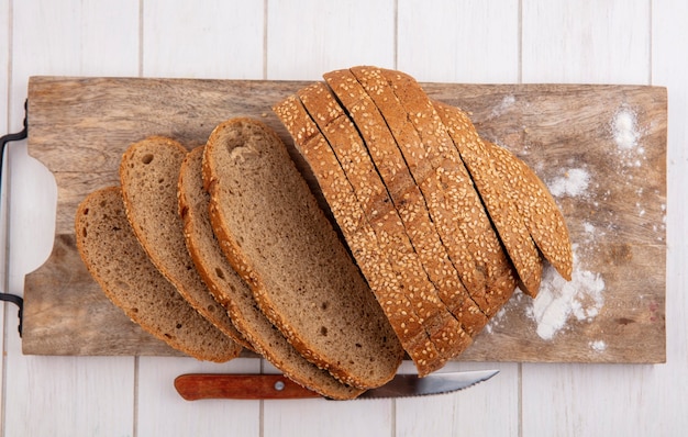 Free photo top view of sliced brown seeded cob on cutting board and knife on wooden background