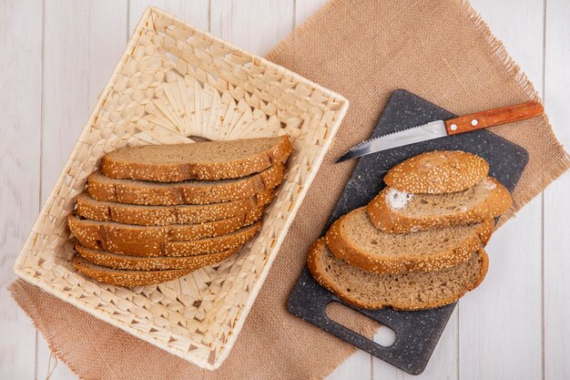 Top view of sliced brown seeded cobs in basket and on cutting board with knife on sackcloth on wooden background