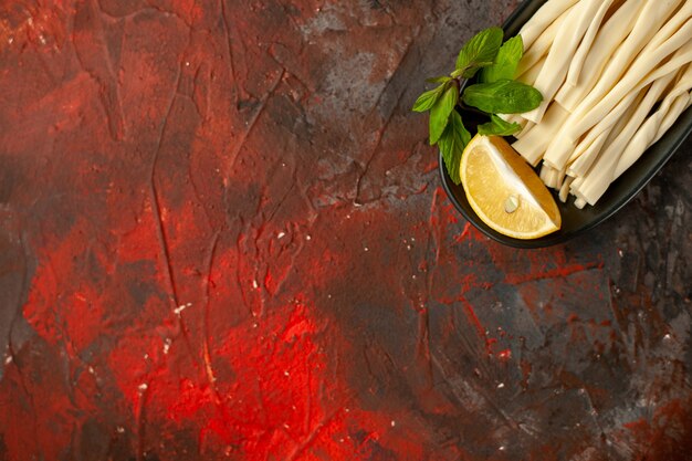 Top view sliced cheese with lemon piece inside plate on dark background