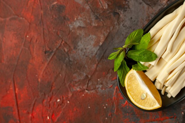 Top view sliced cheese with lemon piece inside plate on dark background