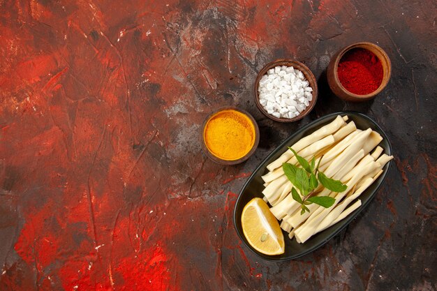 Top view sliced cheese with lemon piece and seasonings on a dark background