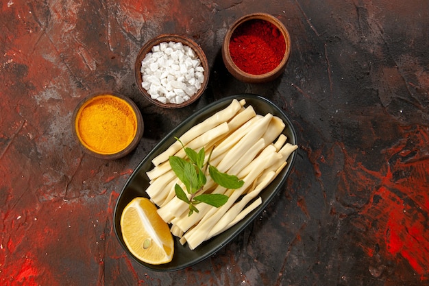 Top view sliced cheese with lemon piece and seasonings on dark background