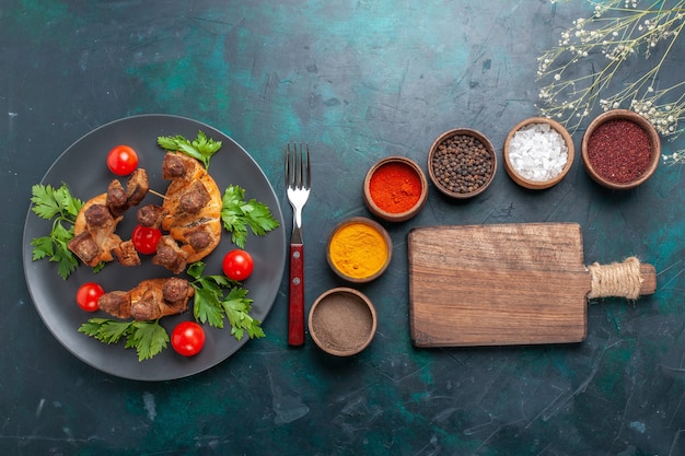 Free photo top view sliced cooked meat with cherry tomatoes and different seasonings on blue background