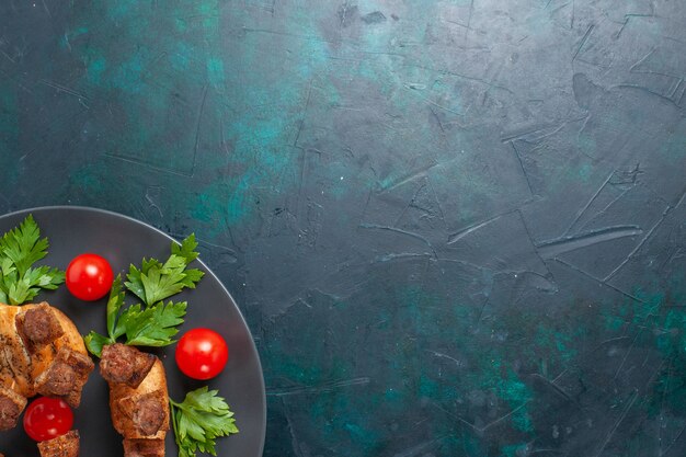 紺色の背景のプレートの内側に緑のチェリートマトとスライスした調理済み肉の上面図