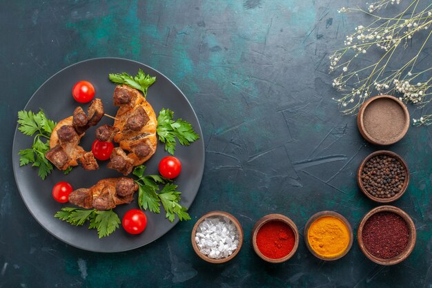 Top view sliced cooked meat with greens and cherry tomatoes with seasonings on blue background