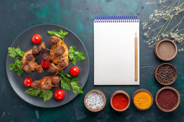 Top view sliced cooked meat with greens and cherry tomatoes with seasonings on the blue background