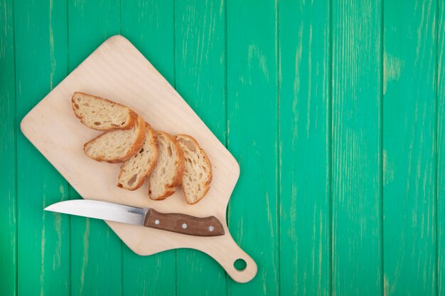 Top view of sliced croissant with knife on cutting board on green background with copy space
