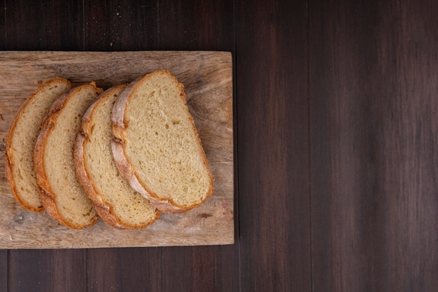 Top view of sliced crusty bread on cutting board on wooden background with copy space