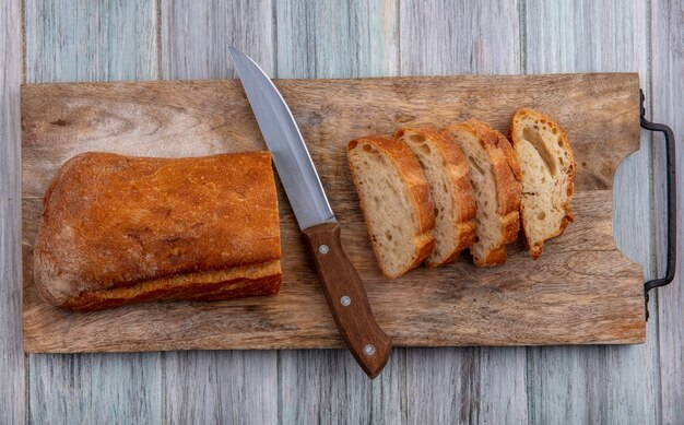 Top view of sliced crusty bread and knife on cutting board on wooden background