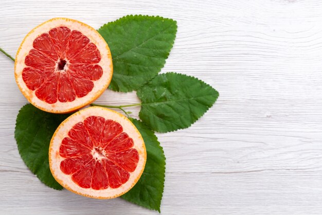 A top view sliced fresh grapefruit along with green leaves on white desk, citrus fruit juice