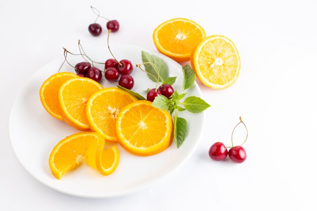 Вид сверху нарезанных свежих апельсинов внутри белой тарелки вместе с красной вишней на белом фоне сока экзотических фруктов