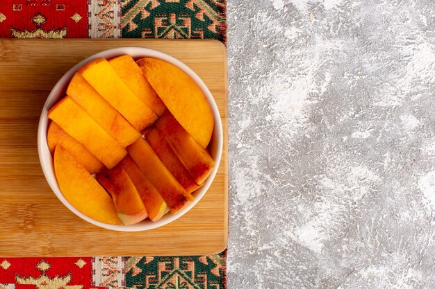 Top view of sliced fresh peaches inside plate on light white surface
