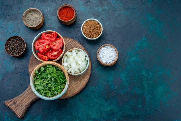 Вид сверху нарезанные свежие овощи, помидоры и лук с зеленью и приправами на темно-синем столе, обед, ужин, овощ