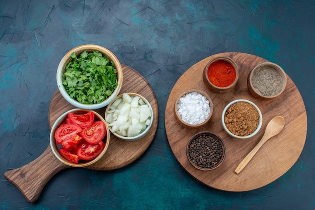 Top view sliced fresh vegetables tomatoes and onions with greens seasonings on dark-blue desk food dinner vegetable dish