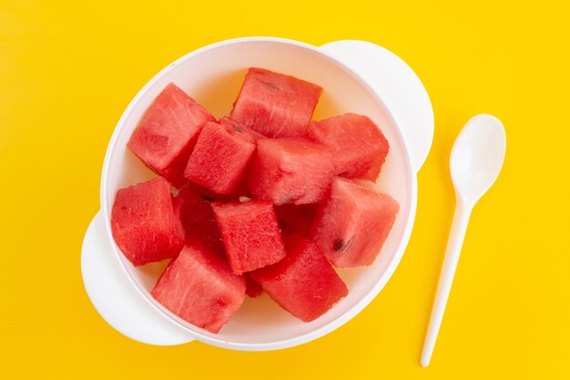 黄色の机、フルーツの夏の色の白いプラスチックプレート内の新鮮なスイカをスライスした平面図