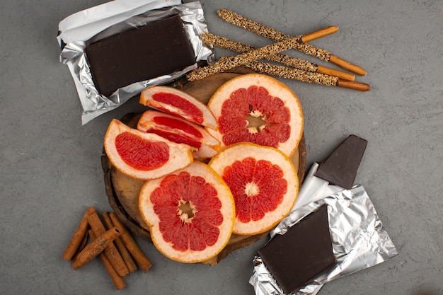 Бесплатное фото Вид сверху нарезанные грейпфруты с шоколадной плиткой и корицей на сером фоне