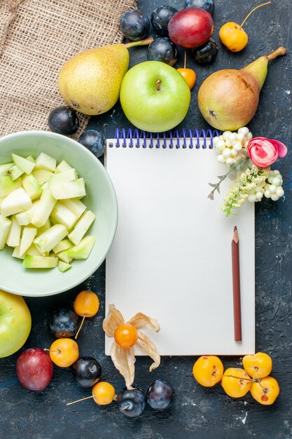 Top view sliced green apple along with different fresh fruits and notepad on the dark-blue desk fruit cookie biscuit sweet fresh