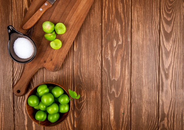 木製のまな板に塩と包丁でスライスされた緑の梅とコピースペースを持つ素朴な木製のテーブルにボウルに梅の平面図