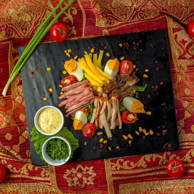 Top view of sliced ham served with eggs tomatoes and sauces on a black board