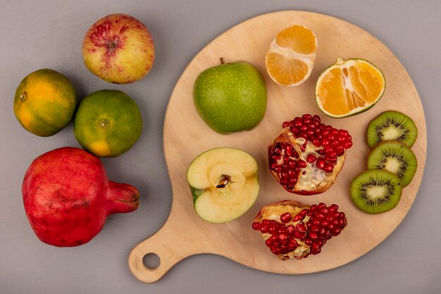Top view of sliced kiwi with halved apple tangerine and pomegranate on a wooden kitchen board