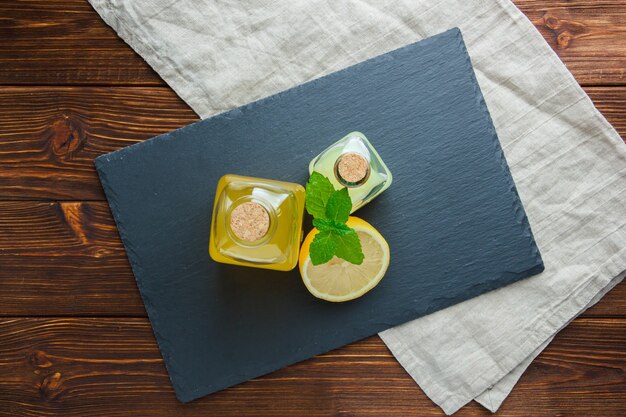 Top view sliced lemon in bowl with black cardboard, juice bottles on wooden surface.