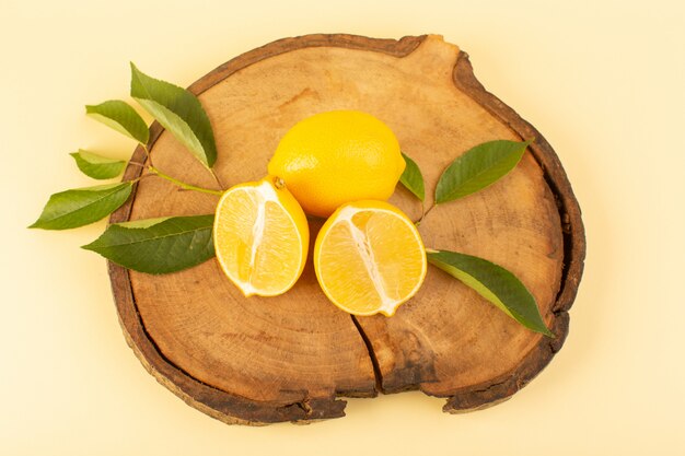 A top view sliced lemon and whole with green leaves on the wooden brown desk isolated fresh juicy mellow on the cream background citrus fruit color