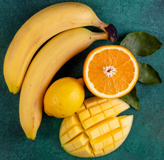 top view sliced mango with bananas half an orange and lemon on green