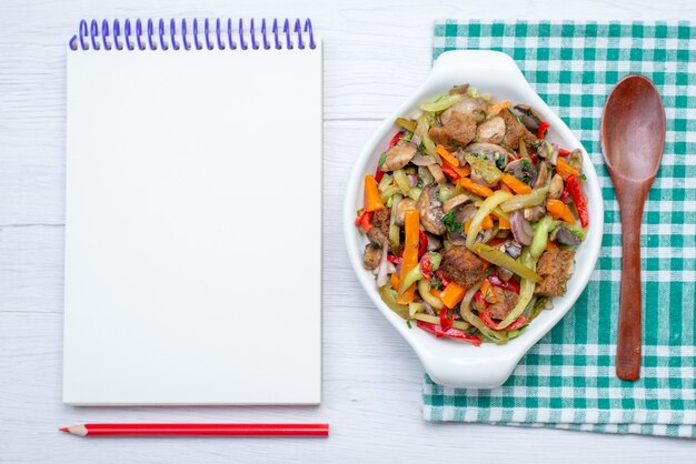 Foto gratuita vista dall'alto piatto di carne a fette con verdure cotte all'interno della piastra insieme al blocco note sulla carne di verdure pasto cibo sfondo chiaro