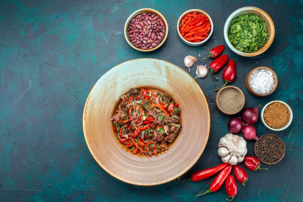 Top view sliced meat with vegetables along with onions garlics greens on the dark-blue desk vegetable food meal ingredient