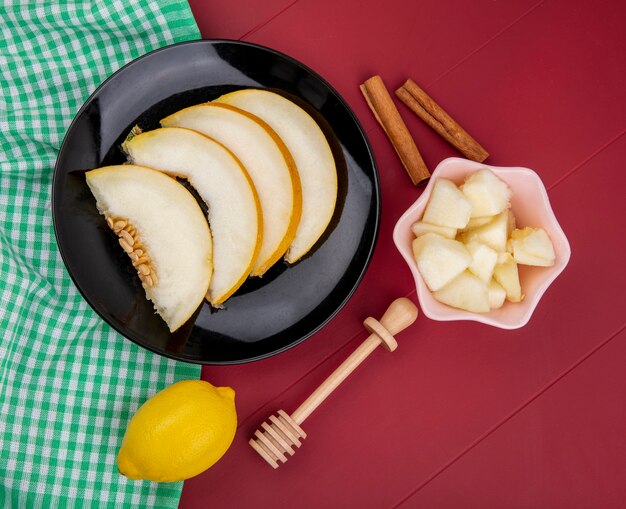 Top view of sliced melon on a black plate with slices of melon on a pink bowl with lemon on red surface