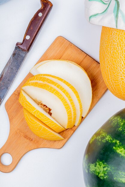 Top view of sliced melon on cutting board with knife and whole one with watermelon on white background