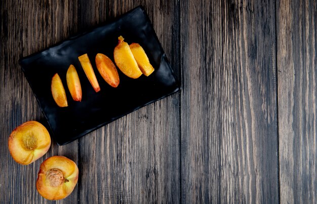 top view of sliced peach on a black tray on rustic wooden background with copy space