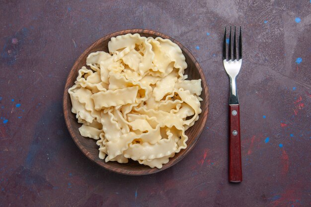 暗い背景の茶色のプレート内のスライスされた生の生地の上面図食事食品夕食パスタ生地