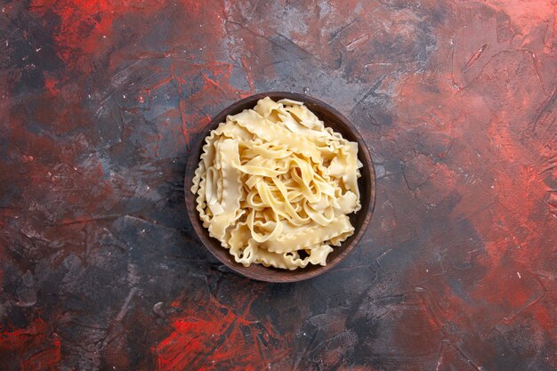 Вид сверху нарезанное сырое тесто внутри тарелки на темной поверхности тесто макароны сырые темные продукты