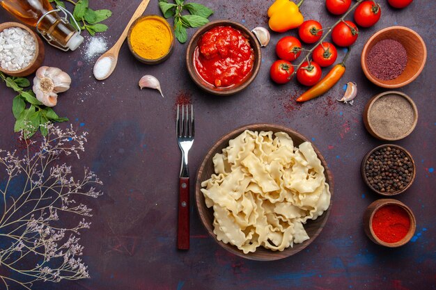 Top view sliced raw dough with tomatoes and seasonings on dark background dough pasta food vegetable