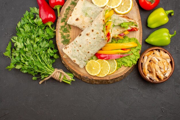 Top view of sliced shaurma meat sandwich with lemon slices and greens on black